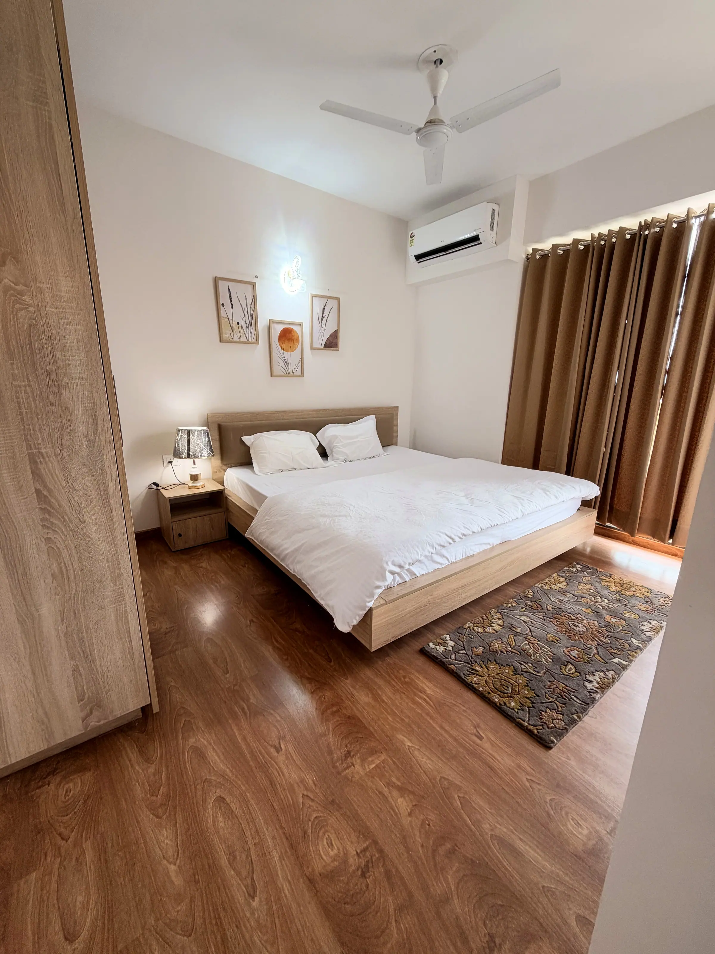 Bedroom one with white linen, three framed botanical prints and a floral rug