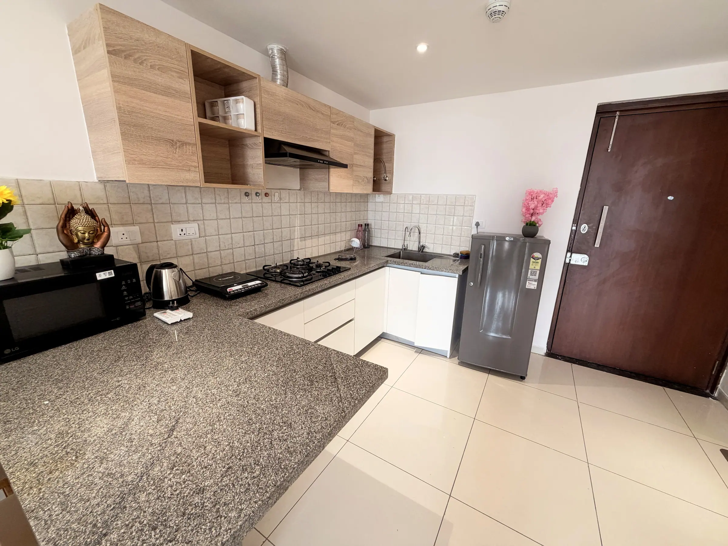 L-shaped kitchen with granite counter, microwave, kettle, induction cooktop, gas hob and refrigerator