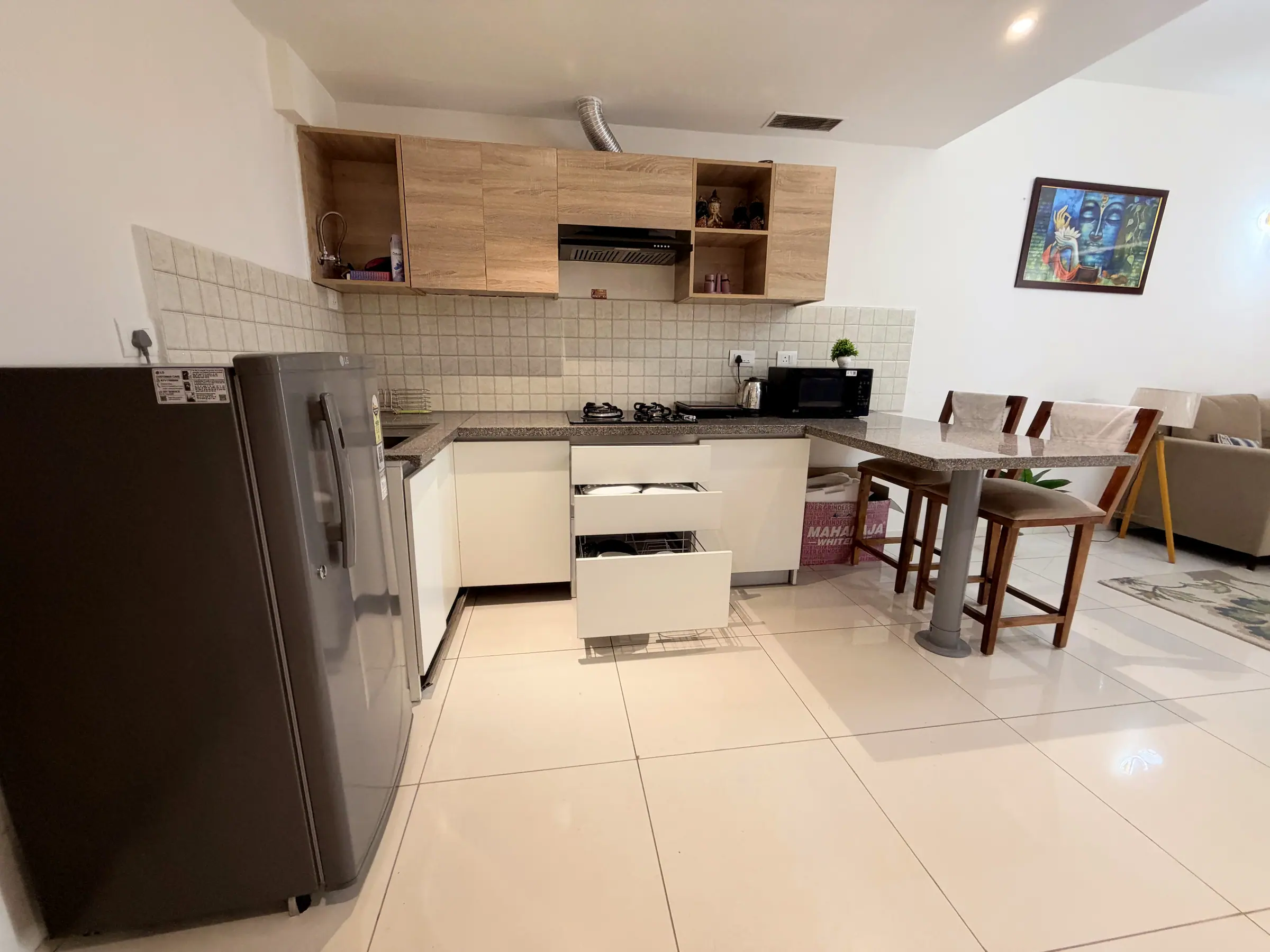 Kitchen with refrigerator, microwave and gas hob beside the breakfast bar and high stools