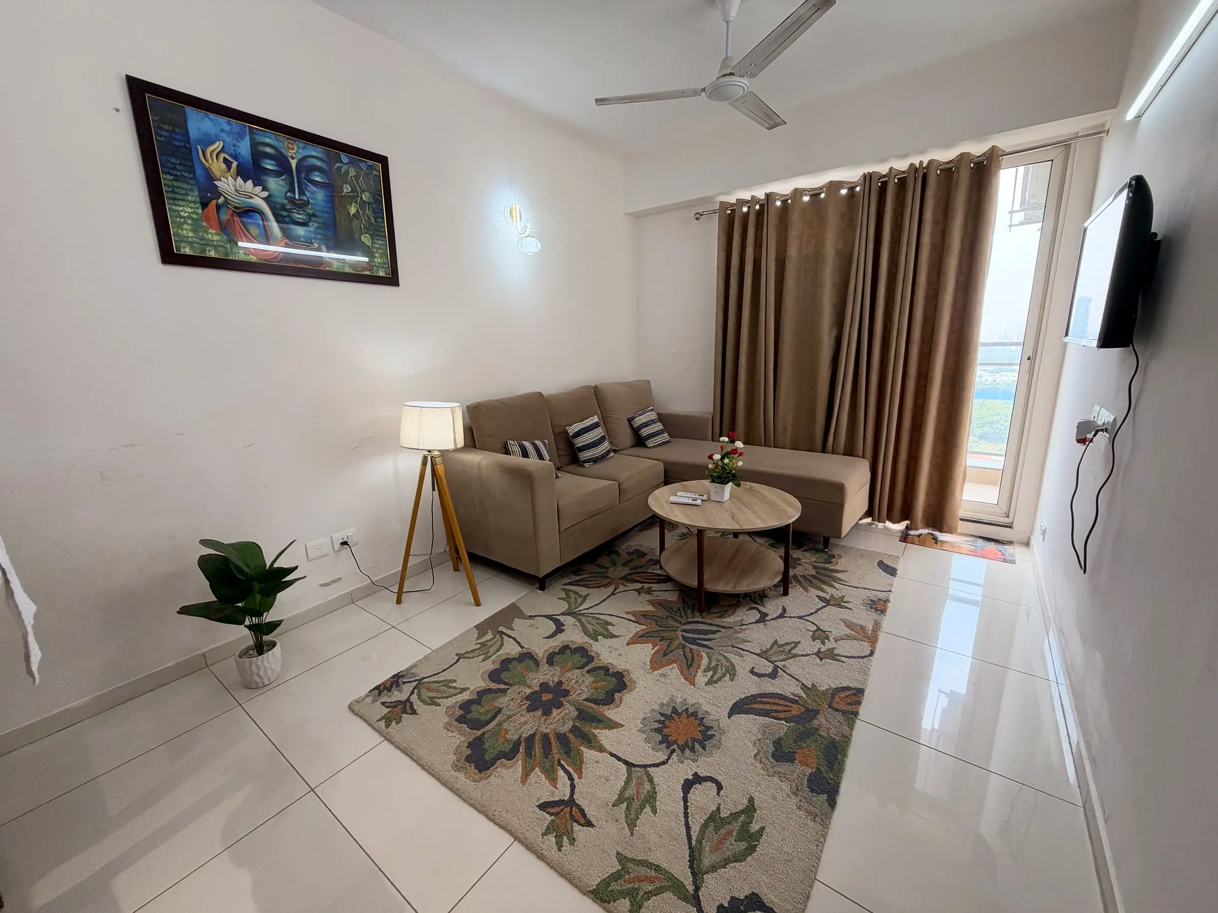 Living room with an L-shaped sofa, round oak coffee table, floral rug, tripod floor lamp and a colourful painting