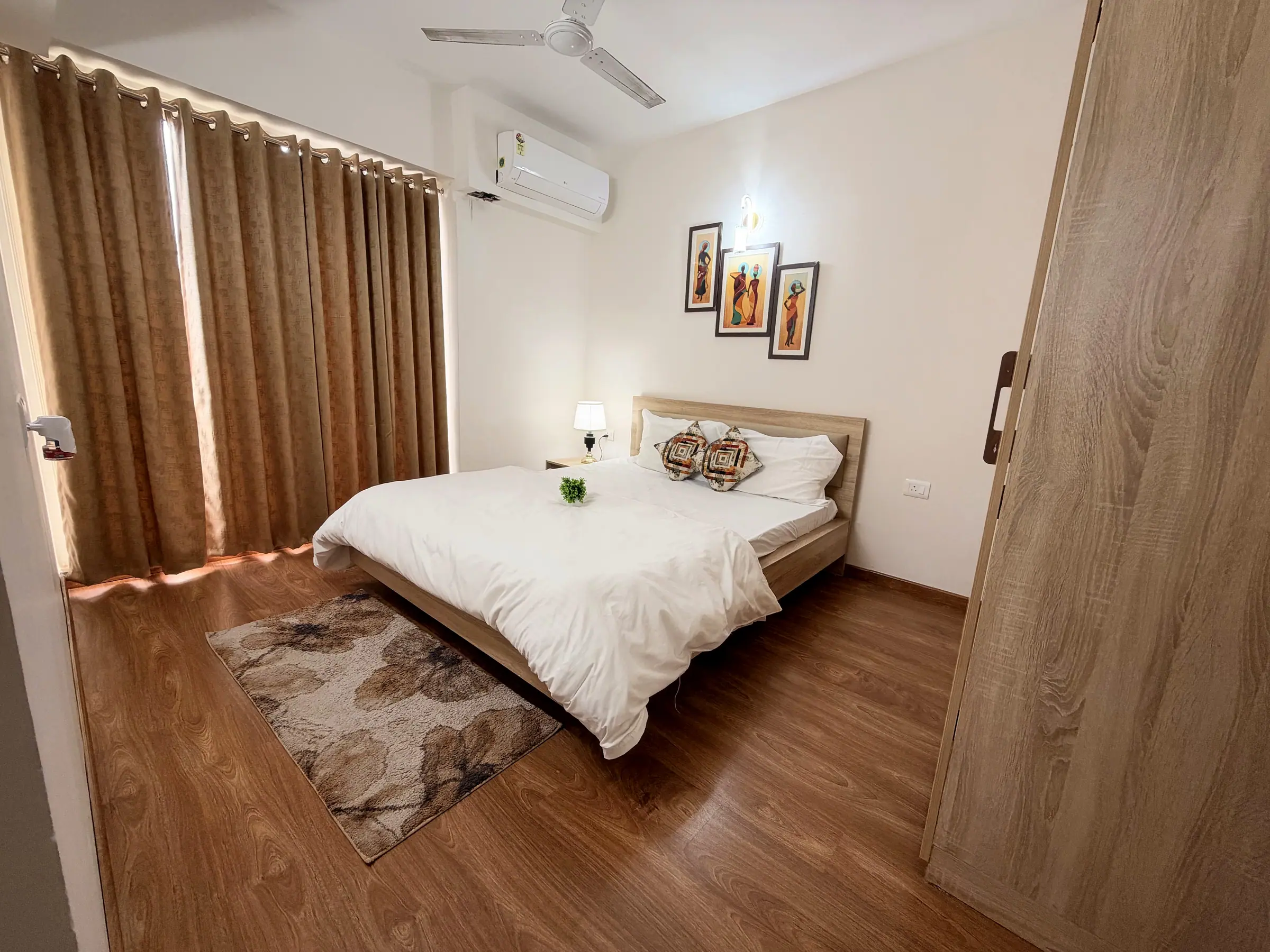 Main bedroom with king bed, patterned cushions, three framed prints and full-length curtains